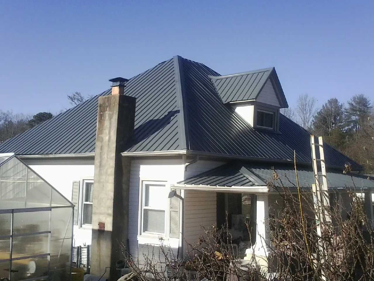 Dark blue standing seam metal roof on a white farmhouse with dormer — Slate & Tile Roof Repair by Roofing Brothers in Scurry