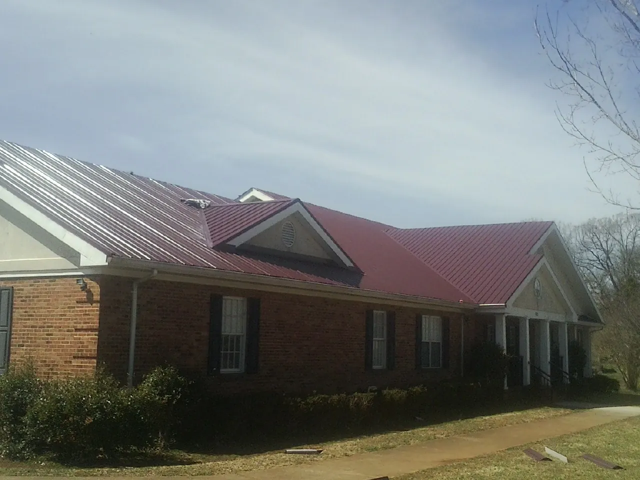 Red metal roof with gabled entries on a long brick building, from a Hail Damage Roof Repair job in Scurry