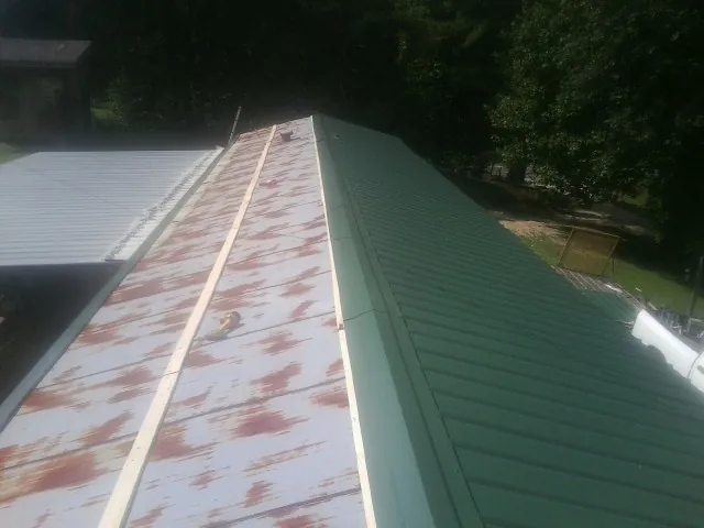Old rusted panels beside newly installed green metal roofing — Wind Damage Roof Repair by Roofing Brothers in Scurry