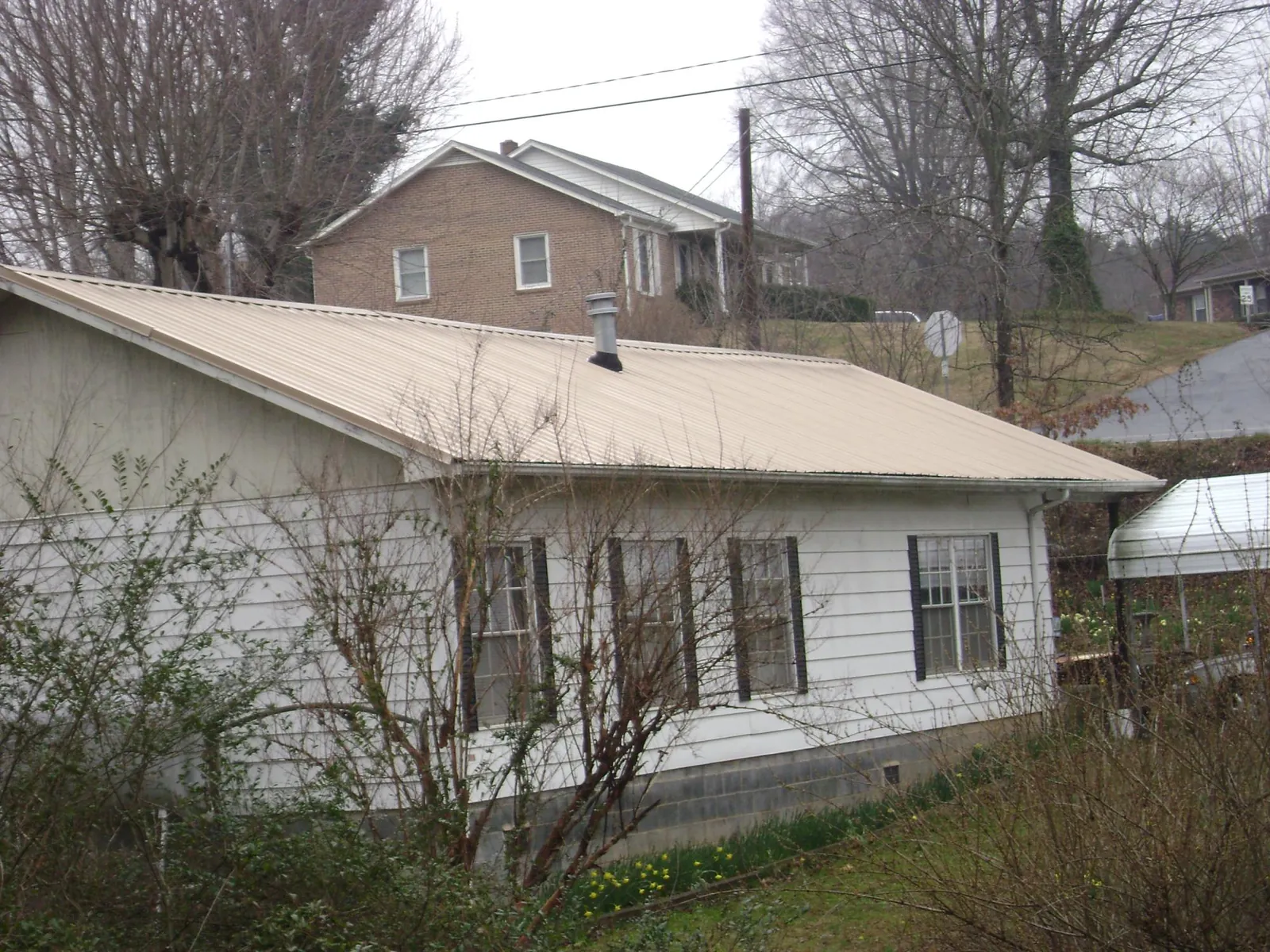 Tan metal roof on a white sided house set into a hillside — Commercial Roofing by Roofing Brothers in Scurry
