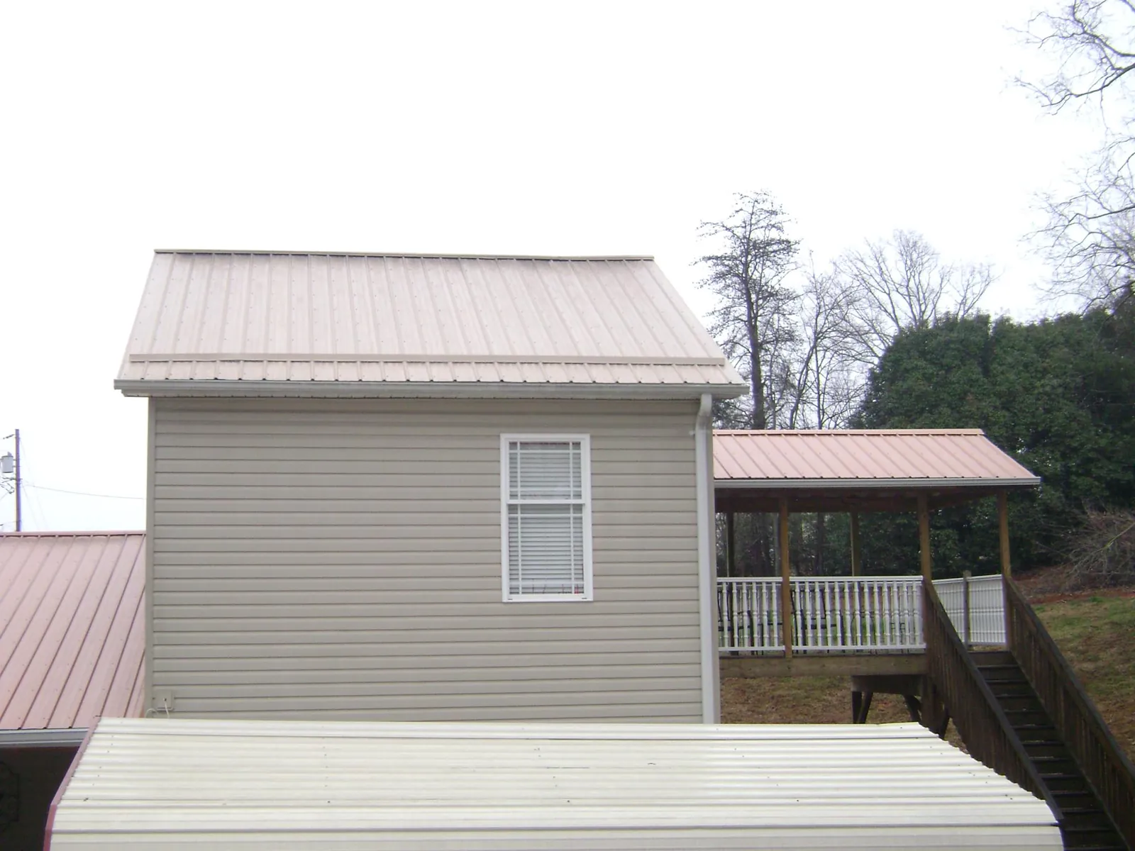 Tan metal roofs on a two story addition and attached porch, from a Roof Replacement job in Scurry